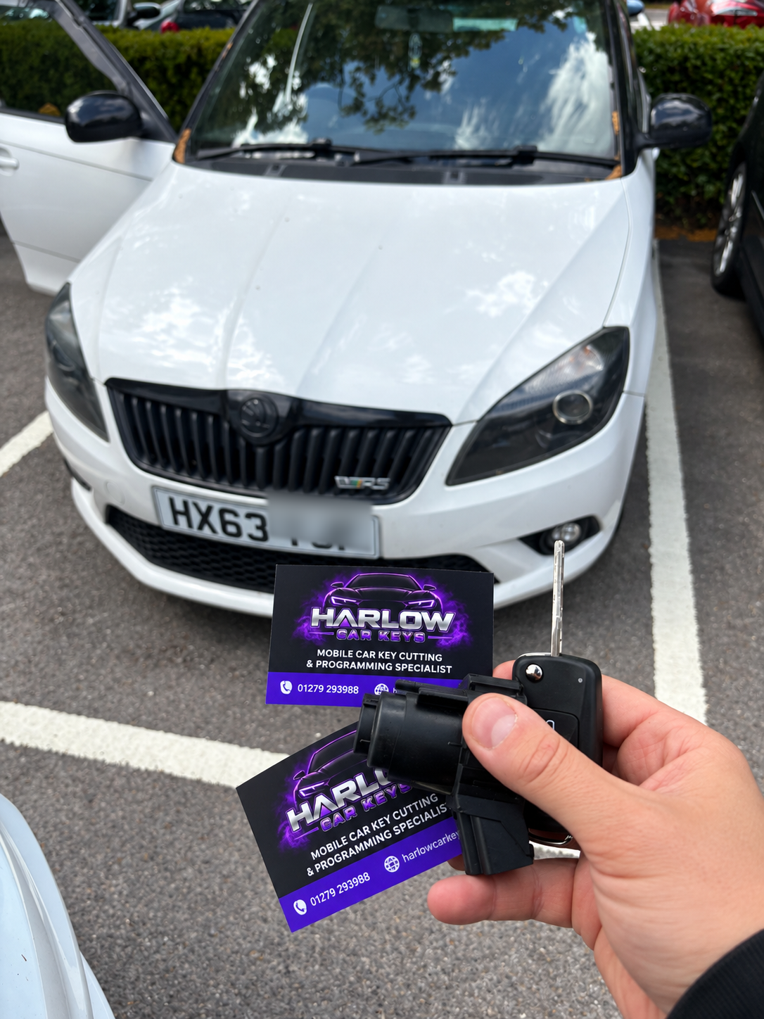 Replacement ignition switch and key case for a 2013 Škoda Fabia in Hertford, held in front of the car with the final three registration characters blurred