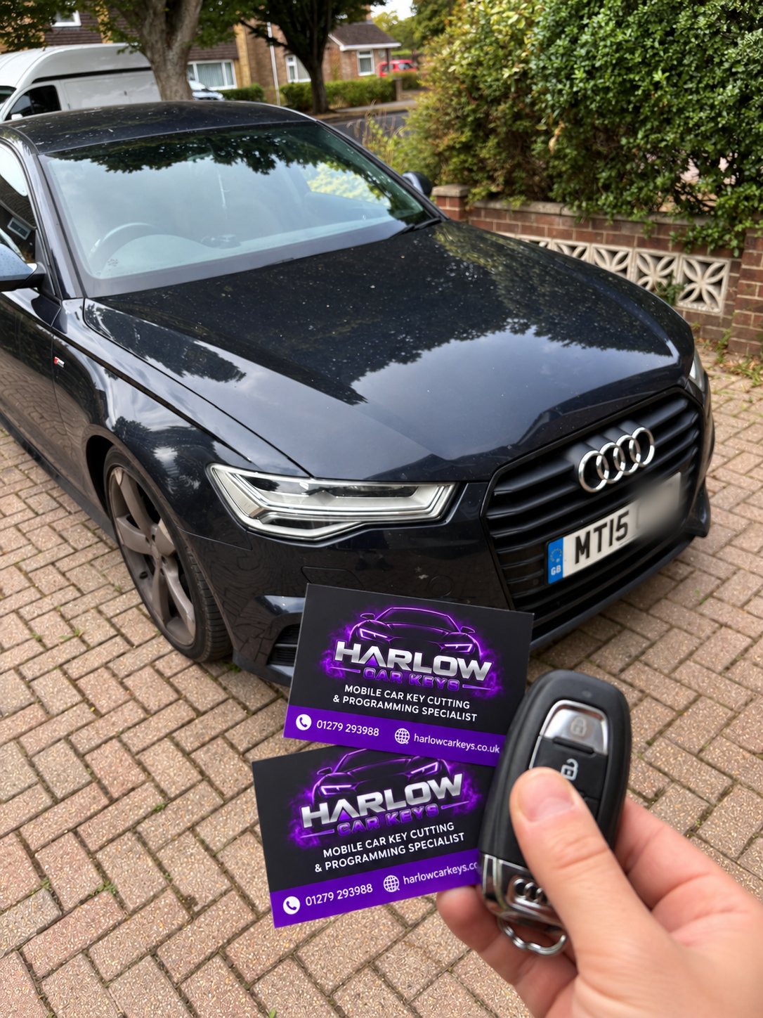 Newly supplied spare key for a 2015 Audi A6, held in front of the customer's car with Harlow Car Keys business cards